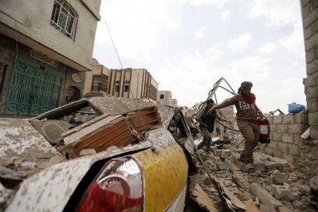 People walk past car damaged by airstrike in Sanaa