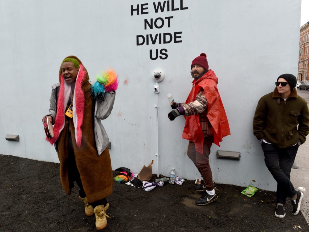 US actor Shia LaBeouf(C) during his He Will Not Divide Us livestream outside the Museum of the Moving Image in Astoria, in the Queens borough of New York January 24, 2017 as a protest against President Donald Trump. LaBeouf has installed a camera at the Museum of the Moving Image in New York that will run a continuous live stream for the duration of Trumps presidency. LaBeouf is inviting the public to participate in the project by saying the phrase, He will not divide us, into the camera. / AFP PHOTO / TIMOTHY A. CLARY