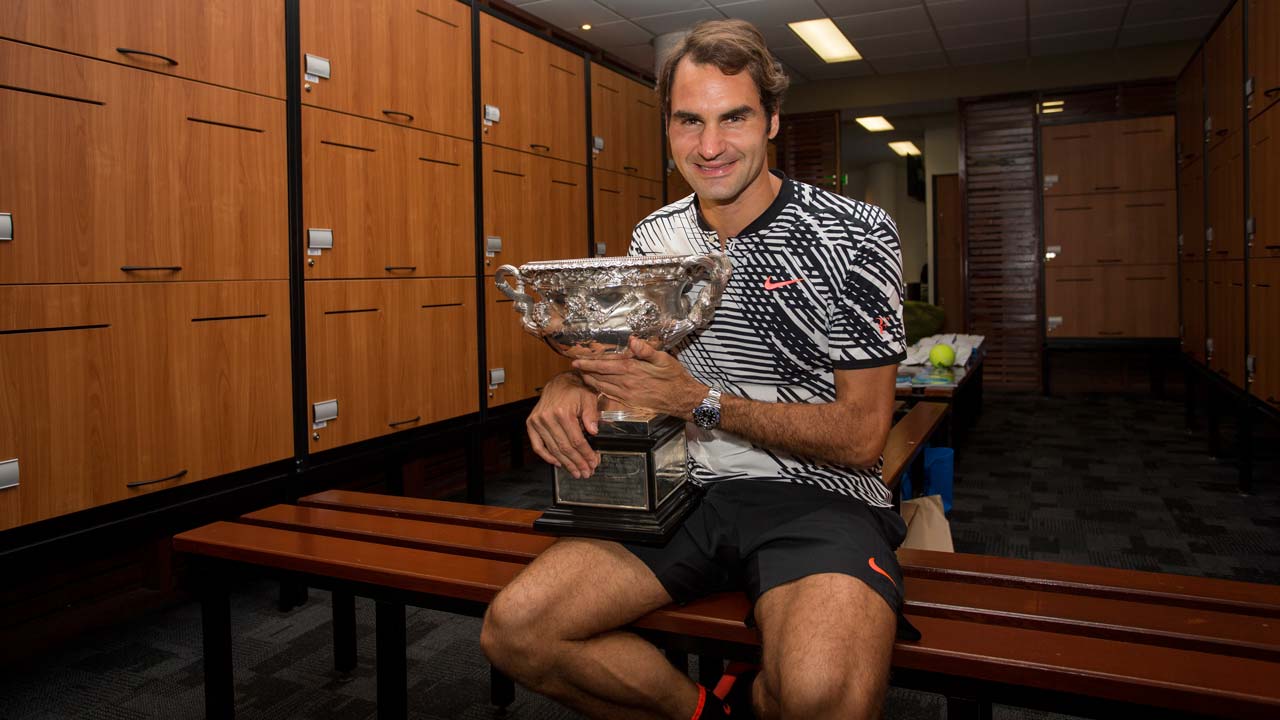 This handout photo taken and released by Tennis Australia on January 30, 2017 shows Switzerland's Roger Federer celebrating with the championship trophy inside the locker room after his victory against Spain's Rafael Nadal in the men's singles final on day 14 of the Australian Open tennis tournament in Melbourne on January 29, 2017. Fiona Hamilton / AFP