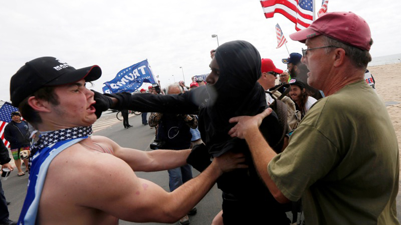 A pro-Trump rally participant is punched in the face by an anti-Trump protester as the two sides clash at a Pro-Trump rally in Huntington Beach