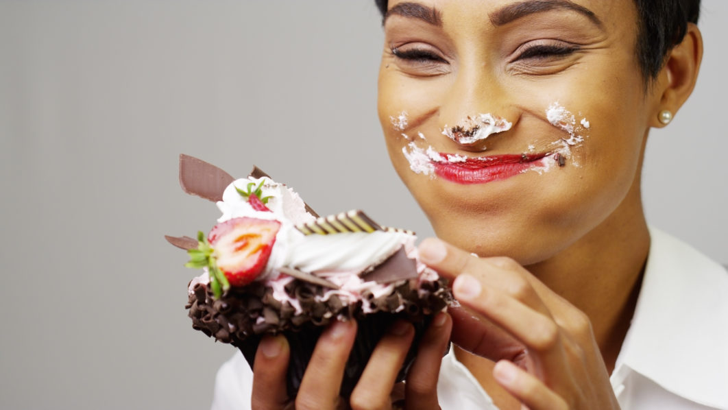 Black woman making a mess eating a huge fancy dessert