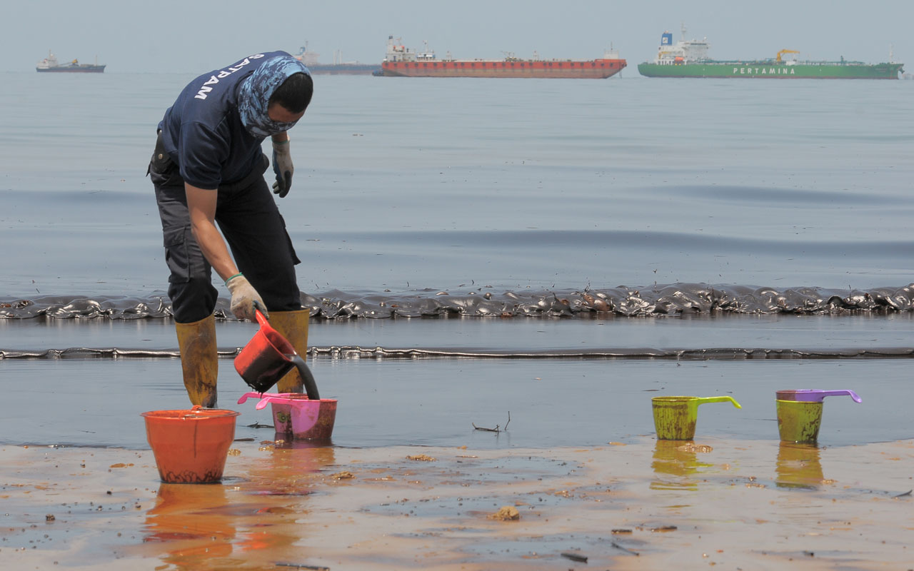 An Indonesian policeman scoops oil polluting Banua Patra beach from an oil spill in the waters off Balikpapan