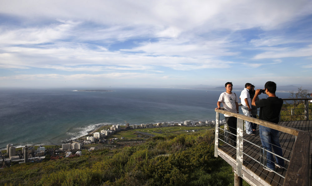 Tourists take pictures from a viewing platform overlooking Cape Town’s Atlantic beachfront and Robben Island