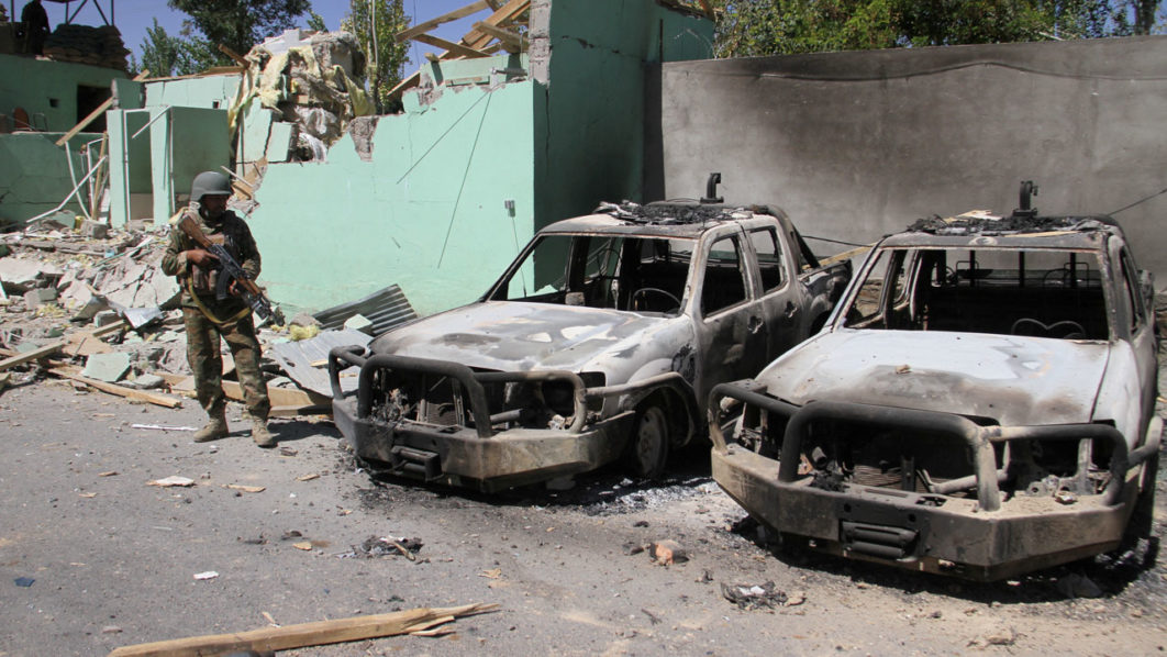 FILE PHOTO: A member of the Afghan security forces stands guard next to damaged army vehicles after a Taliban attack in Ghazni