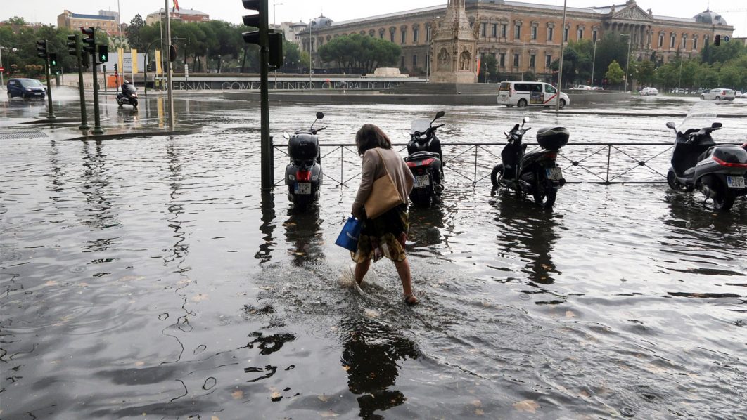 A man runs water on a flooded sidewalk after a downpour in Madrid