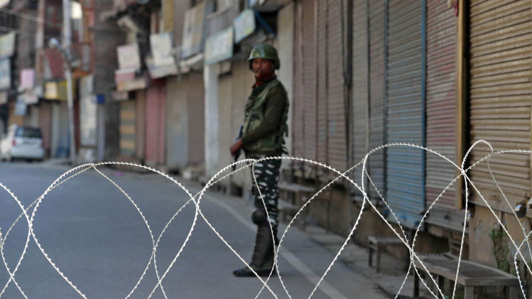 An Indian security force personnel stands guard in front of the closed shops during restrictions, in Srinagar
