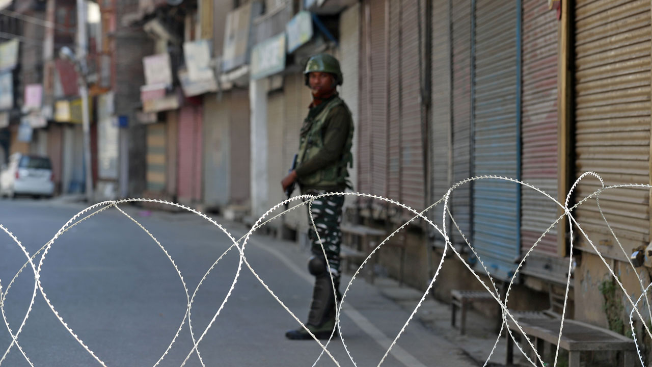 An Indian security force personnel stands guard in front of the closed shops during restrictions, in Srinagar