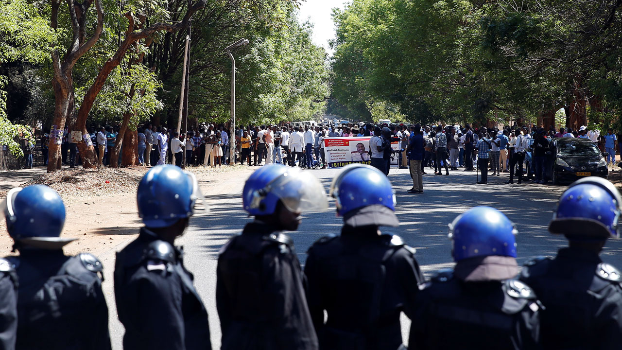 Riot poilce stand before striking healthcare workers protesting over the disappearance of Peter Magombeyi, the leader of their union, outside a hospital in Harare