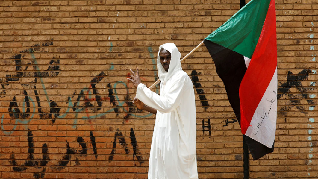 FILE PHOTO: A protester makes victory sign as he carries a Sudanese flag in front of the Defence Ministry in Khartoum