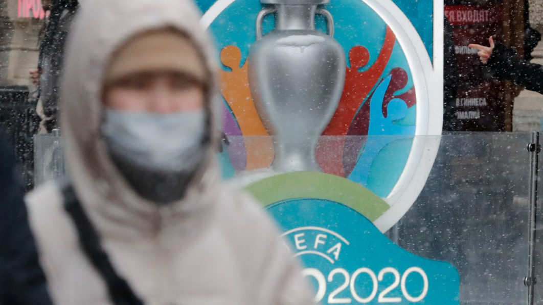 A person wearing a protective face mask walks past the Euro 2020 countdown clock in central Saint Petersburg