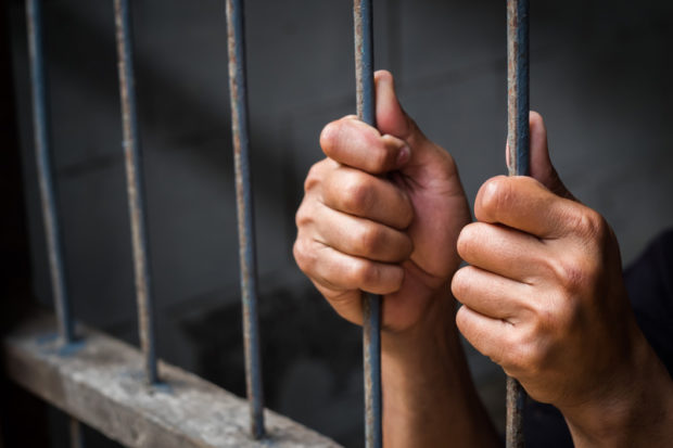 Hands of man behind jail bars.