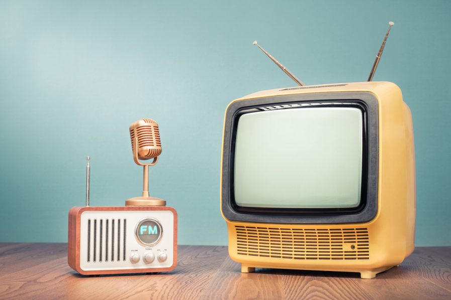 Retro outdated yellow TV set from 70s, old FM radio, classic golden microphone on oak table front mint blue background. News, press conference or nostalgic media concept. Vintage style filtered photo