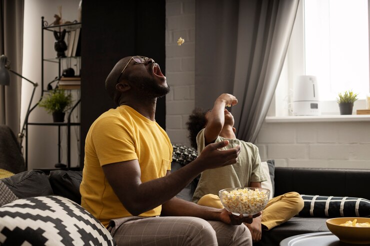 Father and son enjoying popcorn together on the sofa. Photo from Freepik