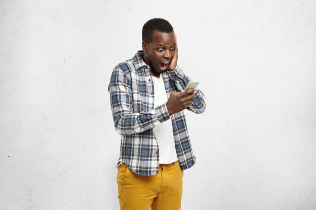 close-up-portrait-black-shocked-hipster-stylish-trendy-yellow-pants-holding-smartphone-one-hand-touching-his-head_273609-564