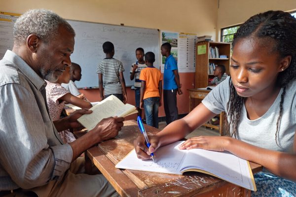 a classroom with an older Nigerian man reading and a younger Nigerian woman besides him