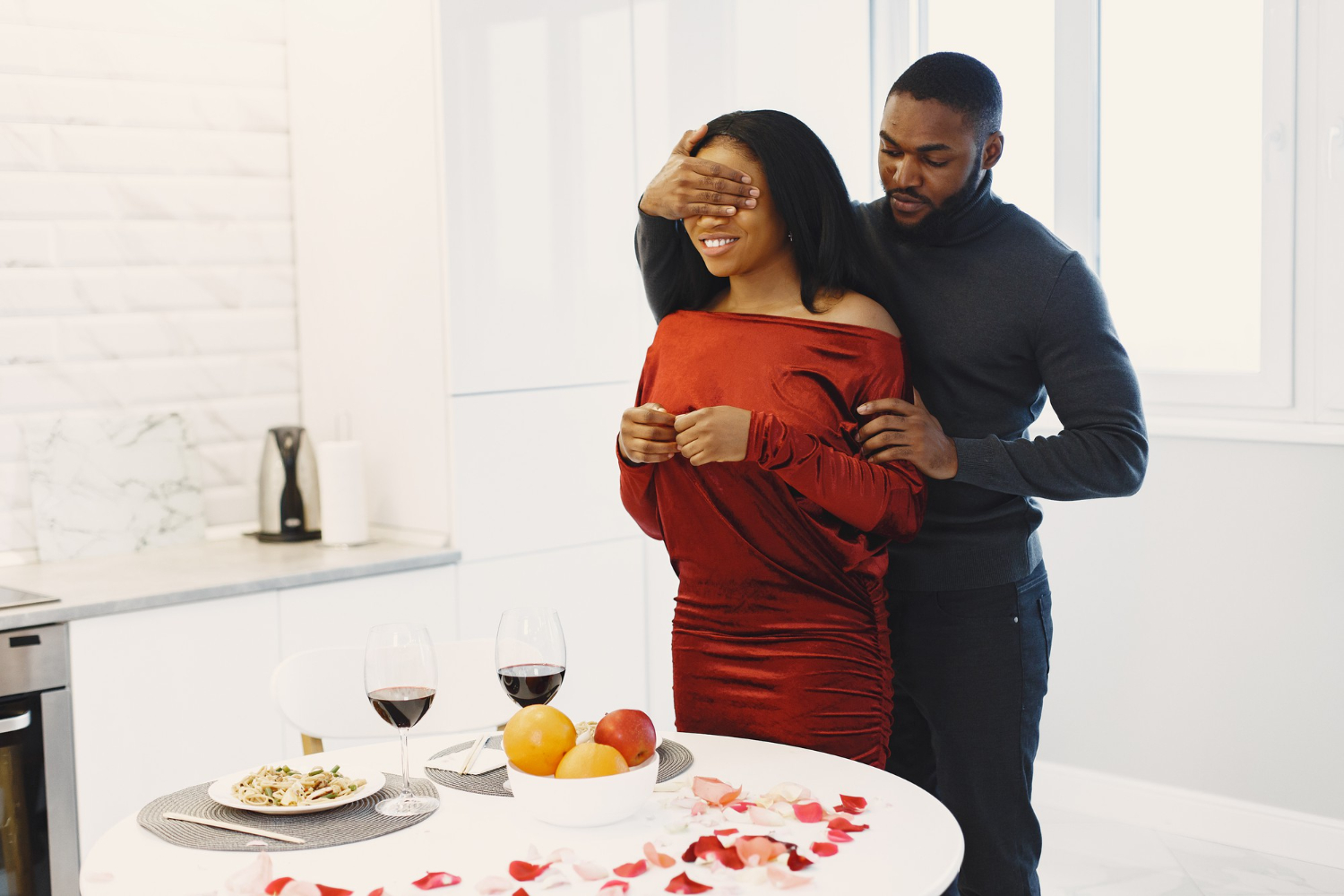 Man surprises his partner with a Valentine dinner at home, with wine, rose petals, and a set table