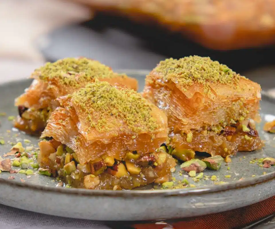 Turkish baklava topped with crushed pistachios, served in pieces on a grey plate