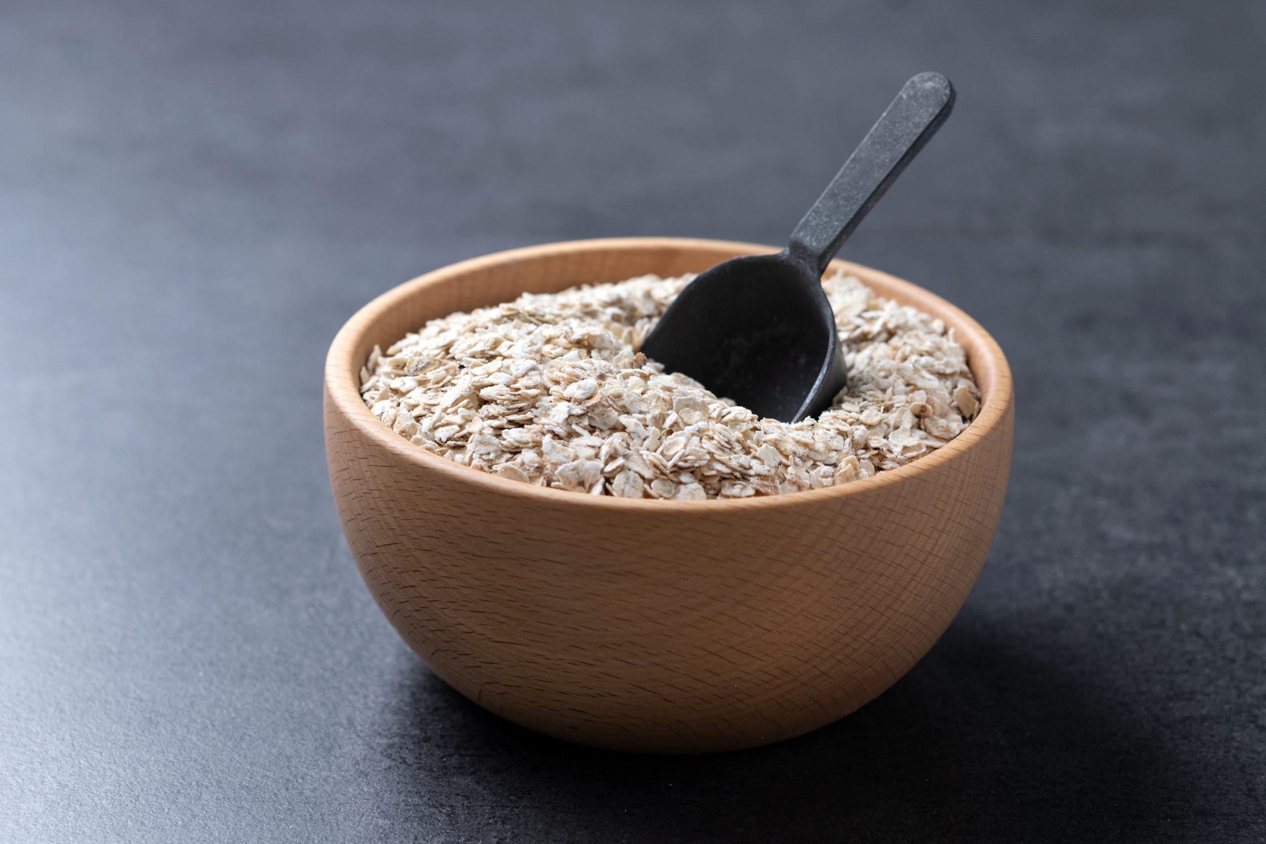 Rolled oats, healthy breakfast cereal oat flakes in bowl on black background