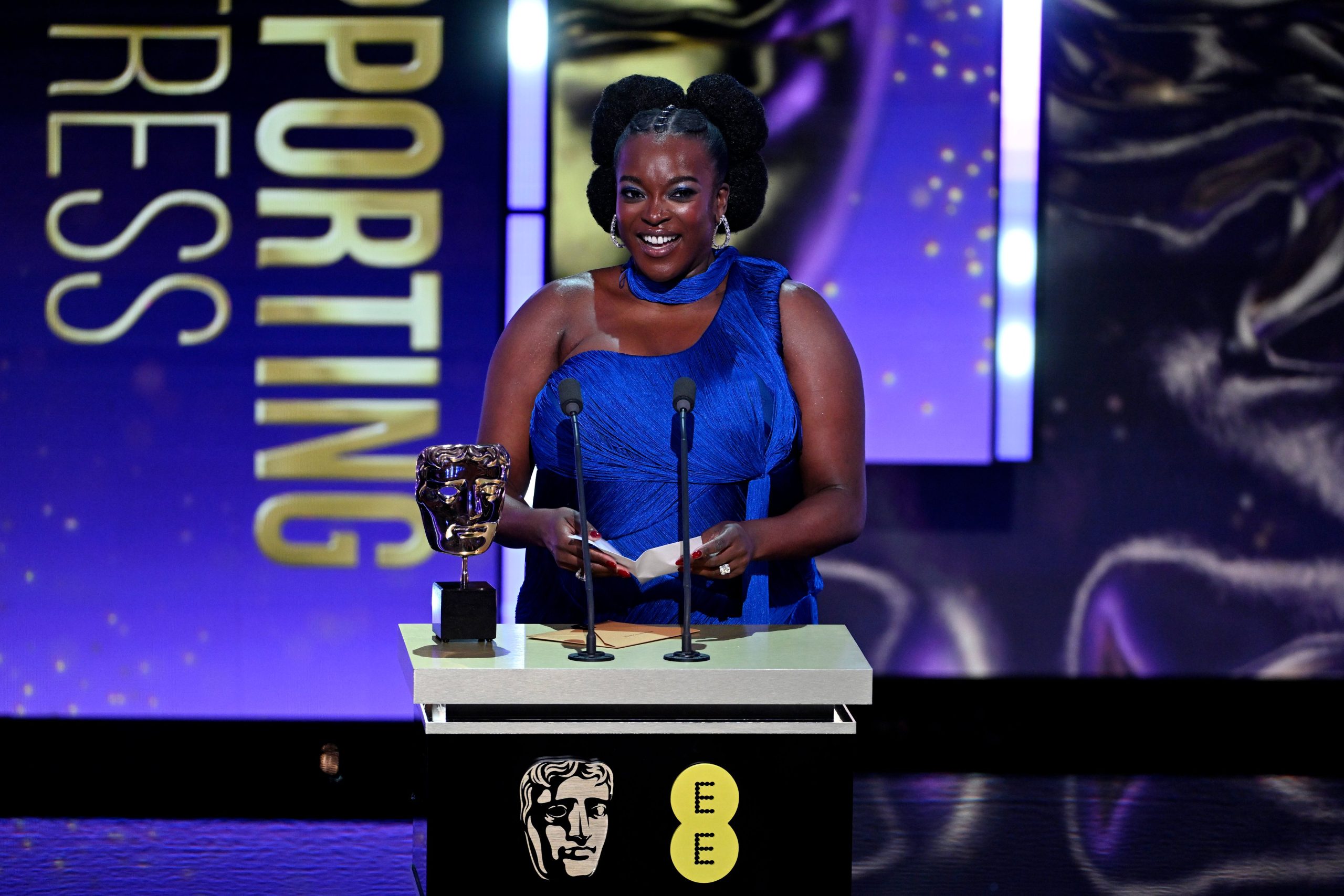 Wunmi Mosaku stands at the BAFTA podium holding notes beside her award after winning best supporting actress for Sinners at the 2026 EE BAFTA Film Awards.