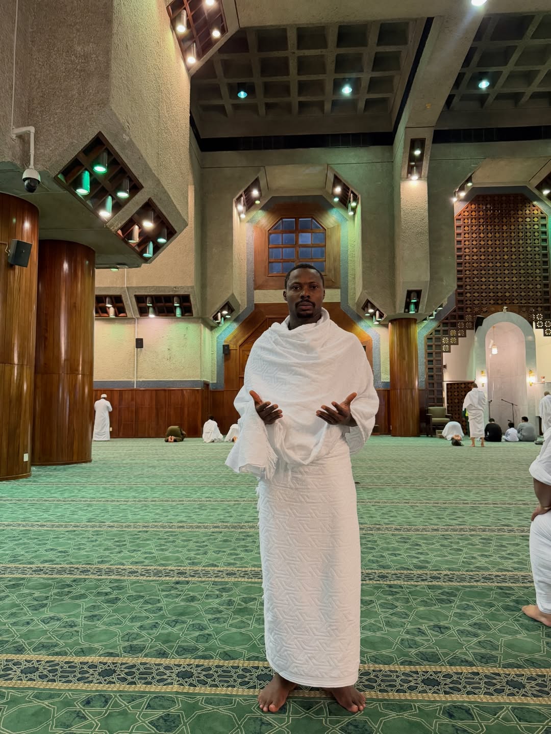 Asake dressed in white ihram praying inside a mosque during Umrah pilgrimage in Mecca