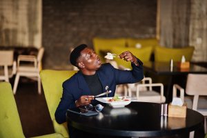 Fashionable african american man in suit sitting at cafe and eat