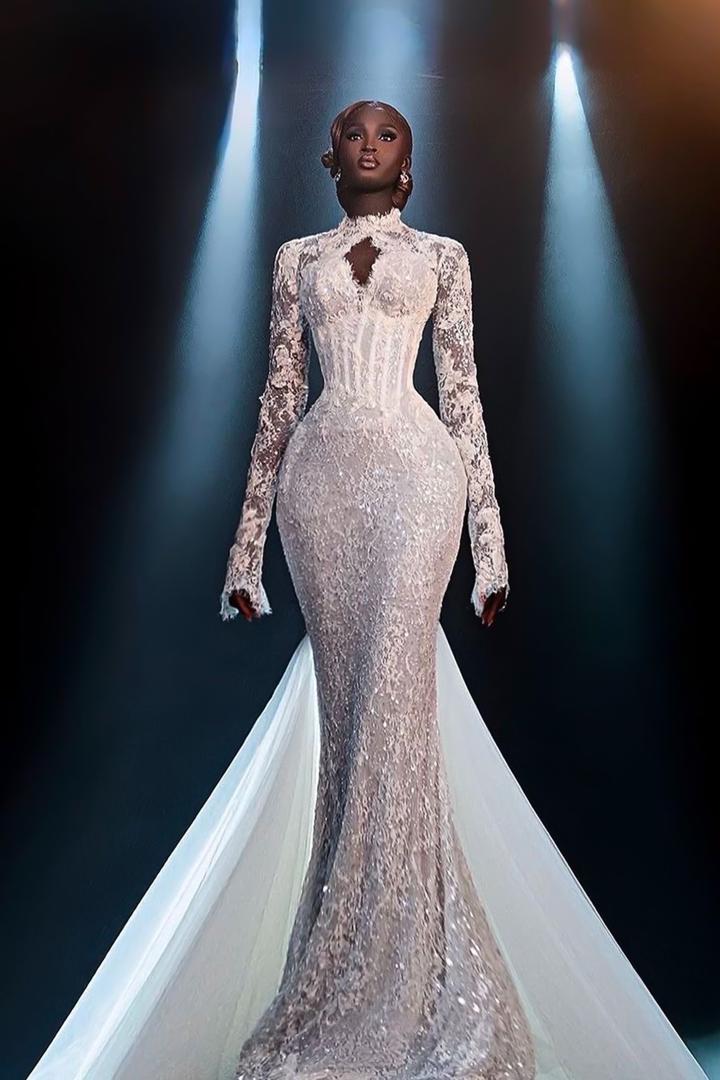 Bride wearing a fitted white lace mermaid wedding gown with long sleeves and dramatic train under spotlight