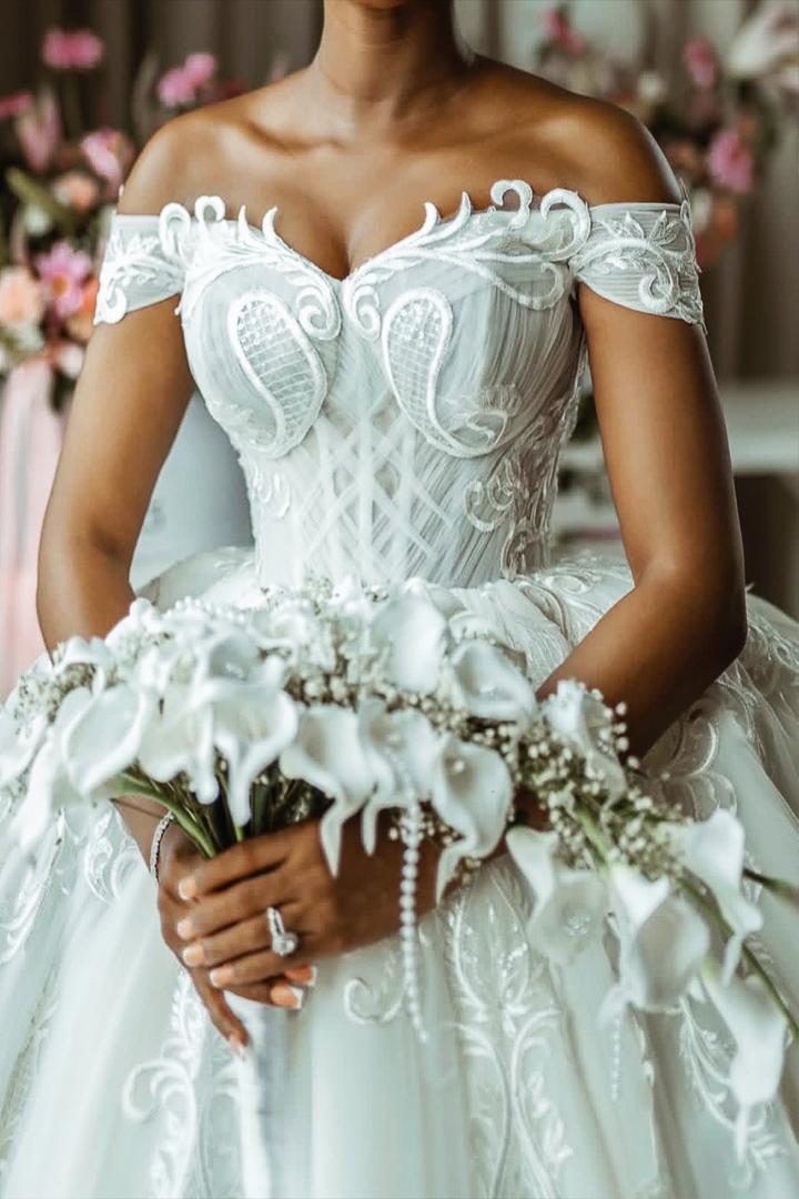 Bride wearing an off shoulder lace wedding gown holding a white floral bouquet with delicate detailing