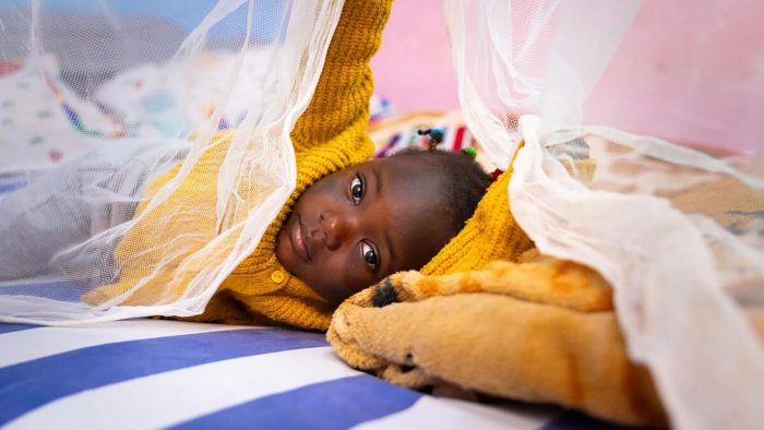 child lying on bed with mosquito net in cameroon