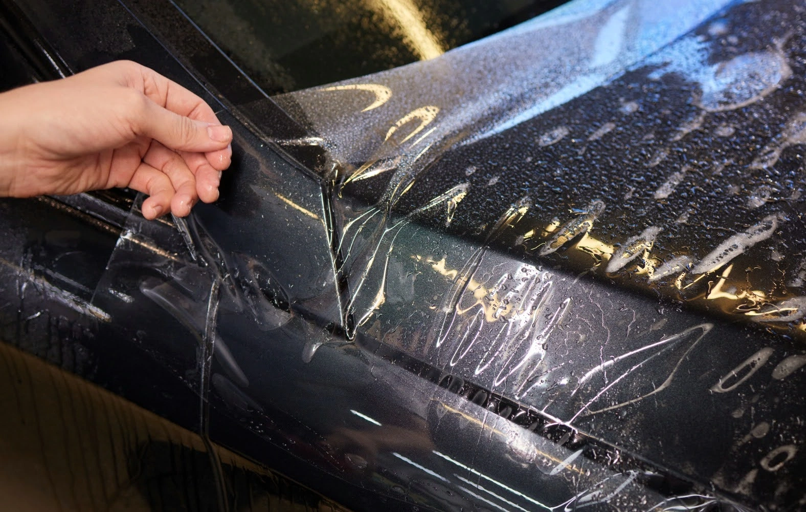 A person applying Paint Protection Film (PPF) on a car.