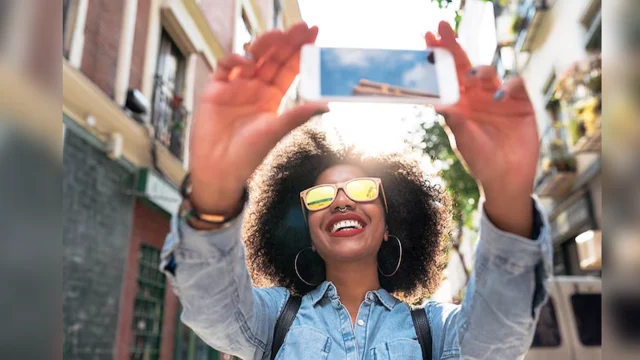 Young beautiful african female traveler with backpack smiling, making selfie at street.