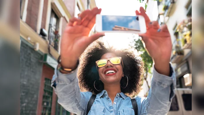Young beautiful african female traveler with backpack smiling, making selfie at street.