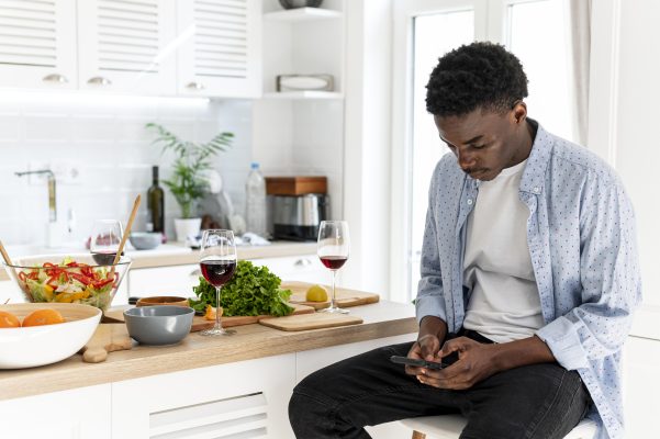 nigerian-man-using-phone-kitchen-healthy-food.jpg