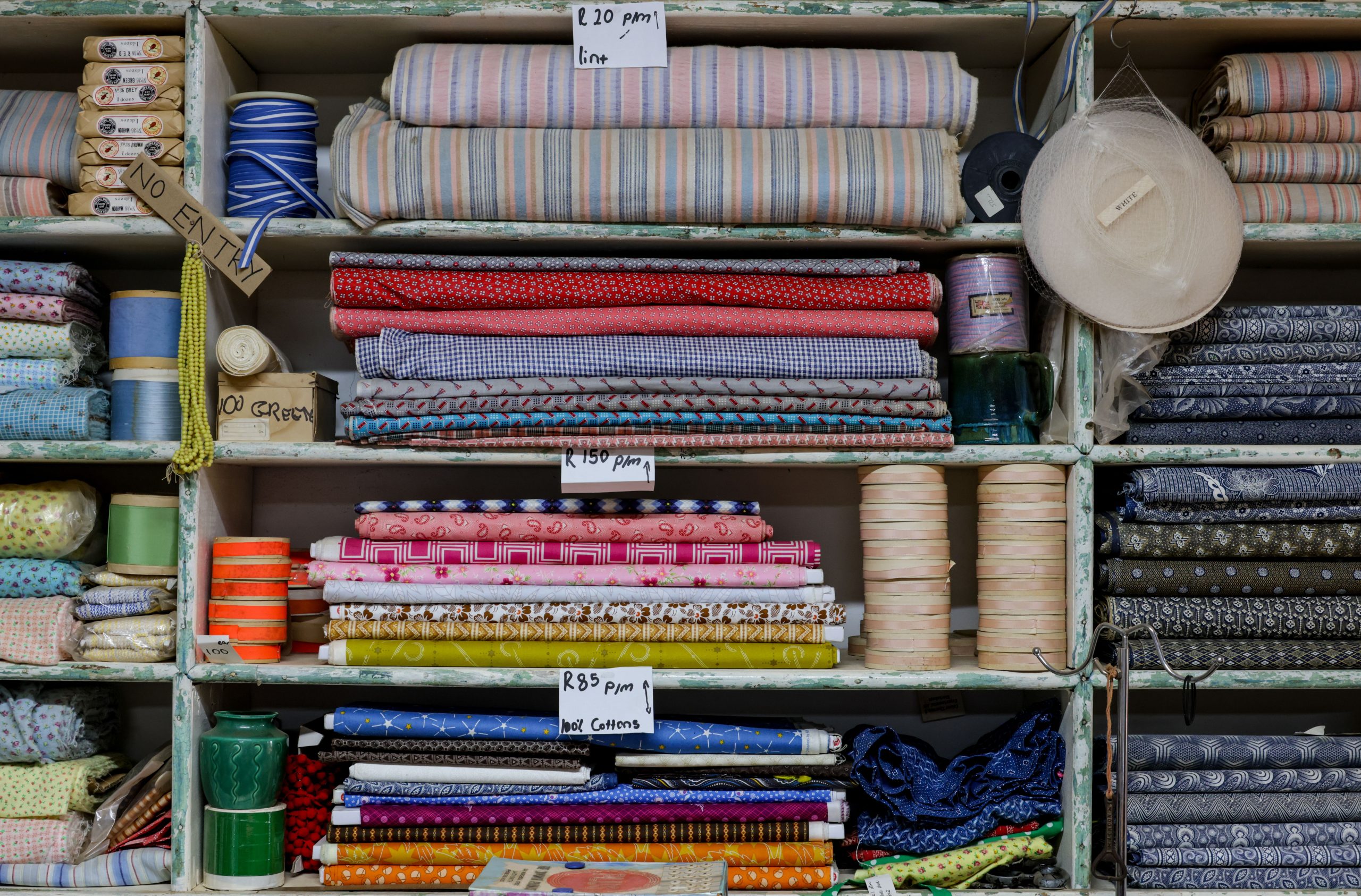 Wooden shelves stocked with colourful folded fabrics, thread spools, ribbons, and sewing notions in an independent fabric shop