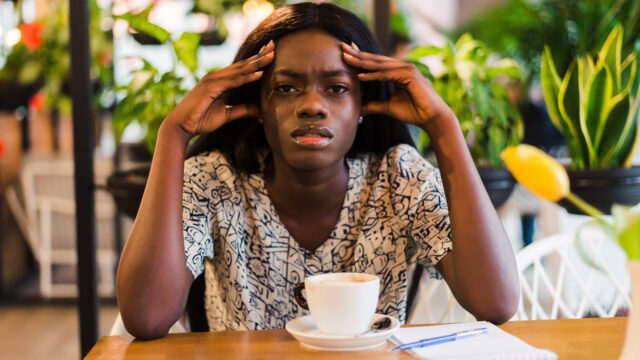 Young woman with coffee cup having headache in cafe