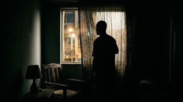 Silhouette of a man behind a curtain in a dimly lit Lagos interior