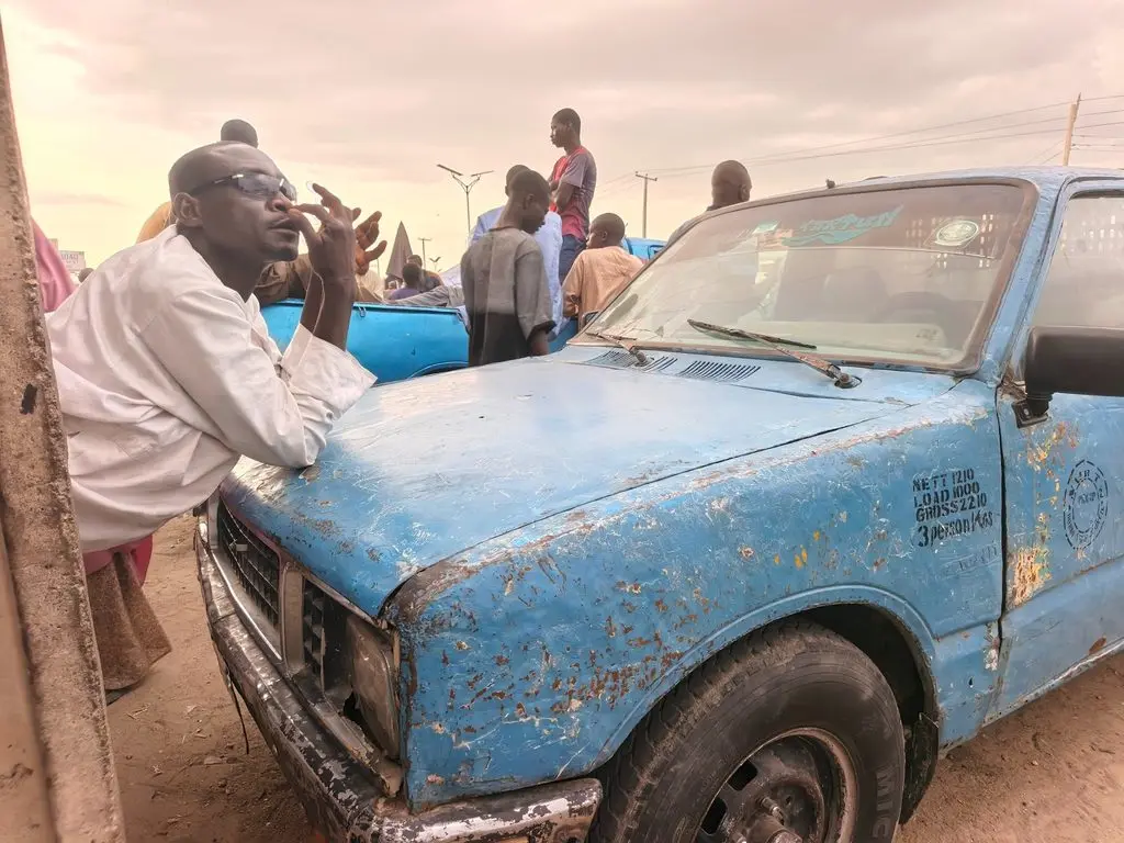 Alkali Muhammed leans against a pickup truck as he recounts his experience travelling along the Maiduguri-Gubio-Damasak-Monguno route. Photo: Al’amin Umar/HumAngle.